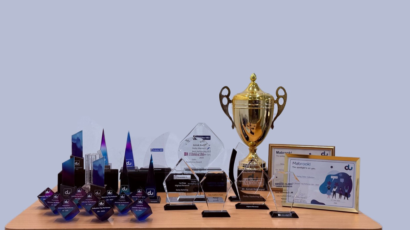 Derby Group's trophy shelf: more than fifty glass and metal industry awards arranged on lit shelving, including several du partner recognitions.